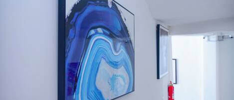 Un pasillo con un cuadro abstracto de gran tamaño en la pared, un extintor y una puerta que da a otra habitación.