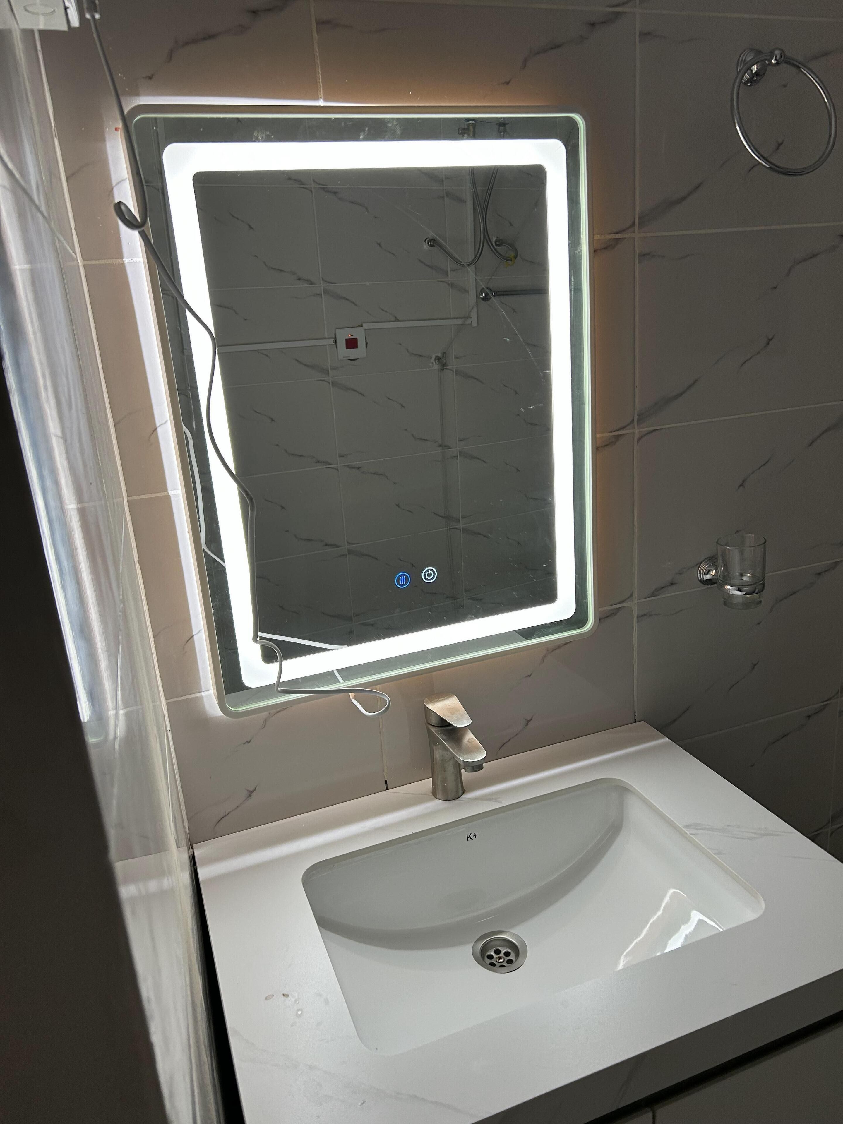 A bathroom with a white sink, a mirror with a light, and a towel ring on the wall.