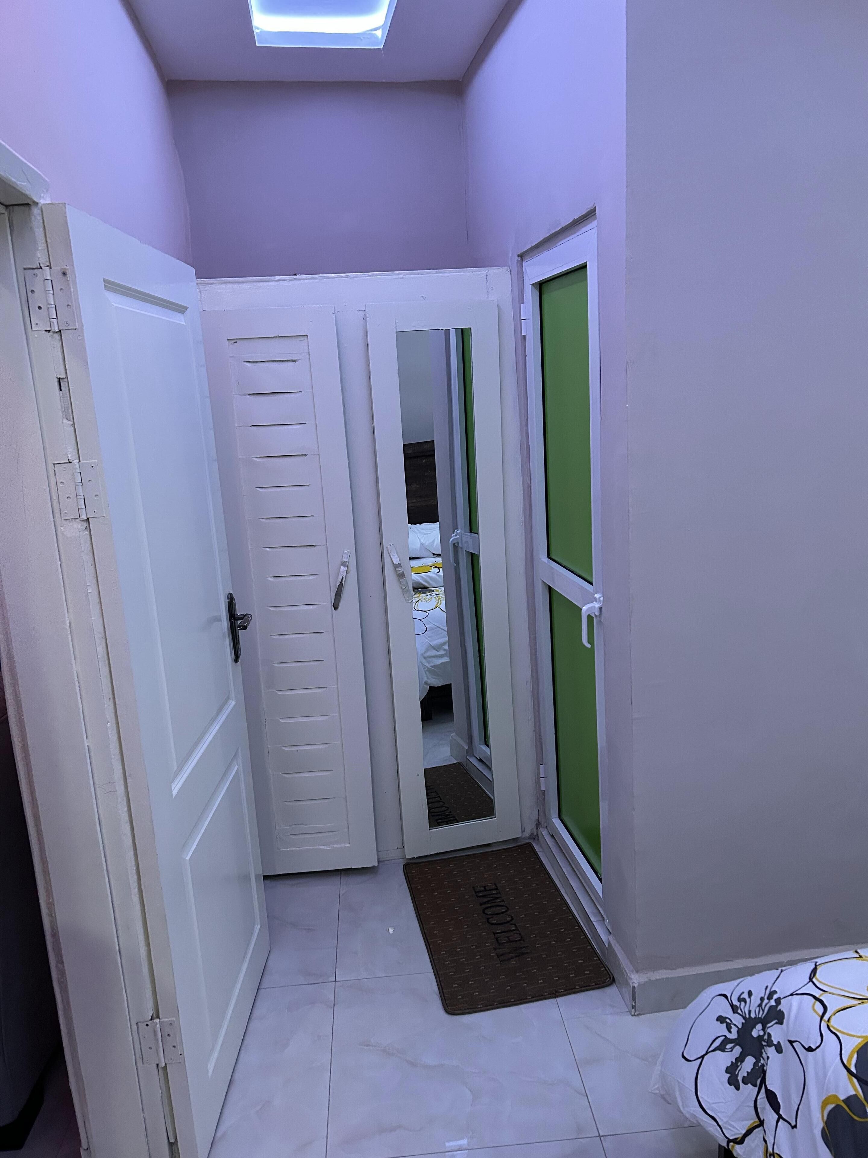 Un pasillo estrecho con puertas blancas, una puerta verde y suelo de baldosas.