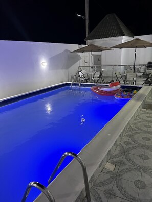 A swimming pool with clear blue water, surrounded by a tiled deck and outdoor furniture. - Legacy Apartments (Brufut)