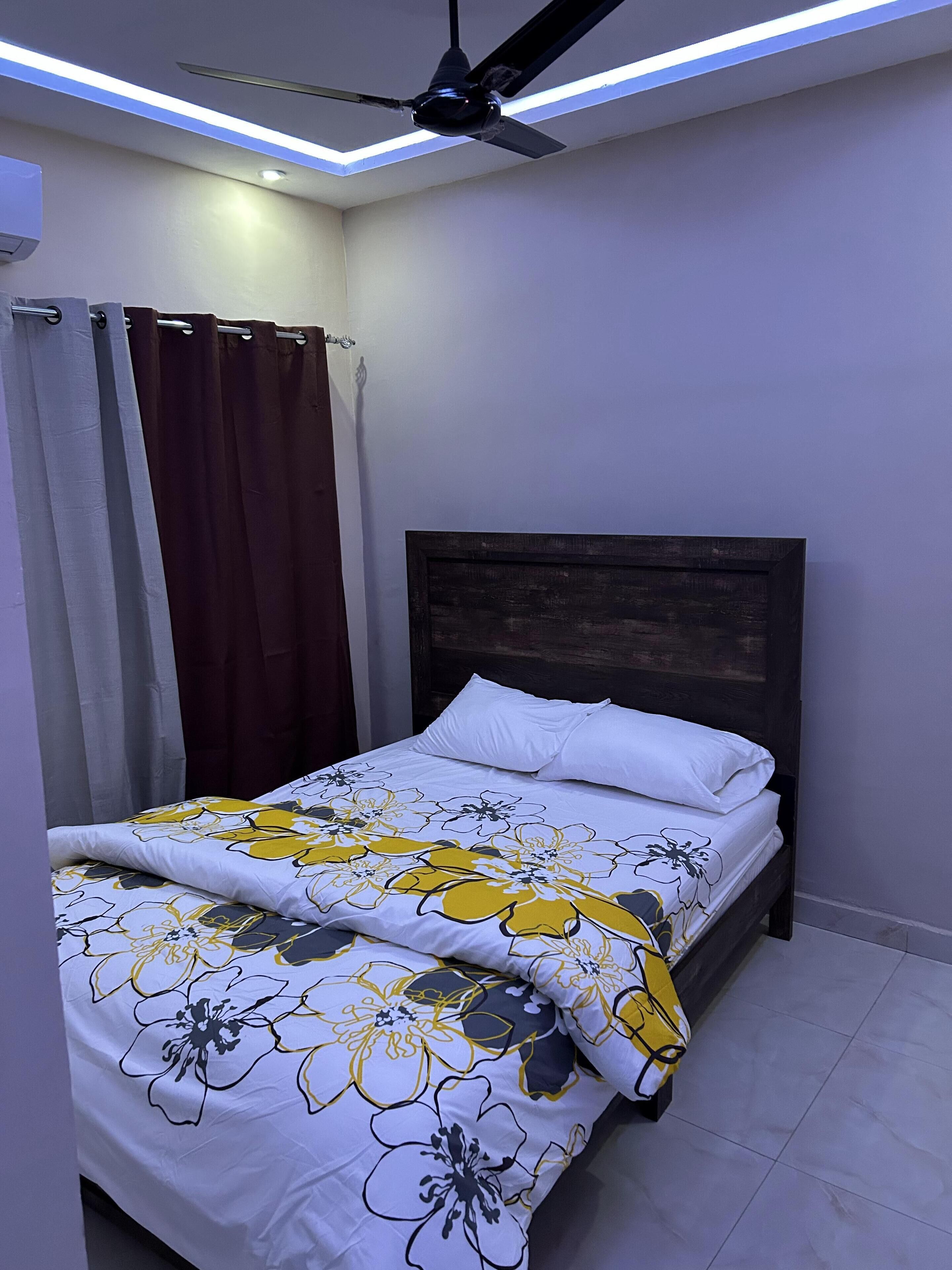 Un dormitori amb llit, cortines, ventilador de sostre i lluminària.