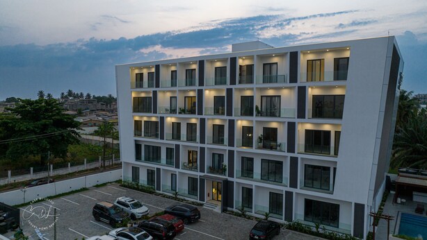 A modern multi-story building with a parking lot in front. - Casse Di Lusso  (Accra)