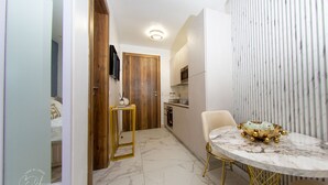 A compact kitchen with a marble countertop, a wooden door, and a small table with a bowl. - Casse Di Lusso  (Accra)