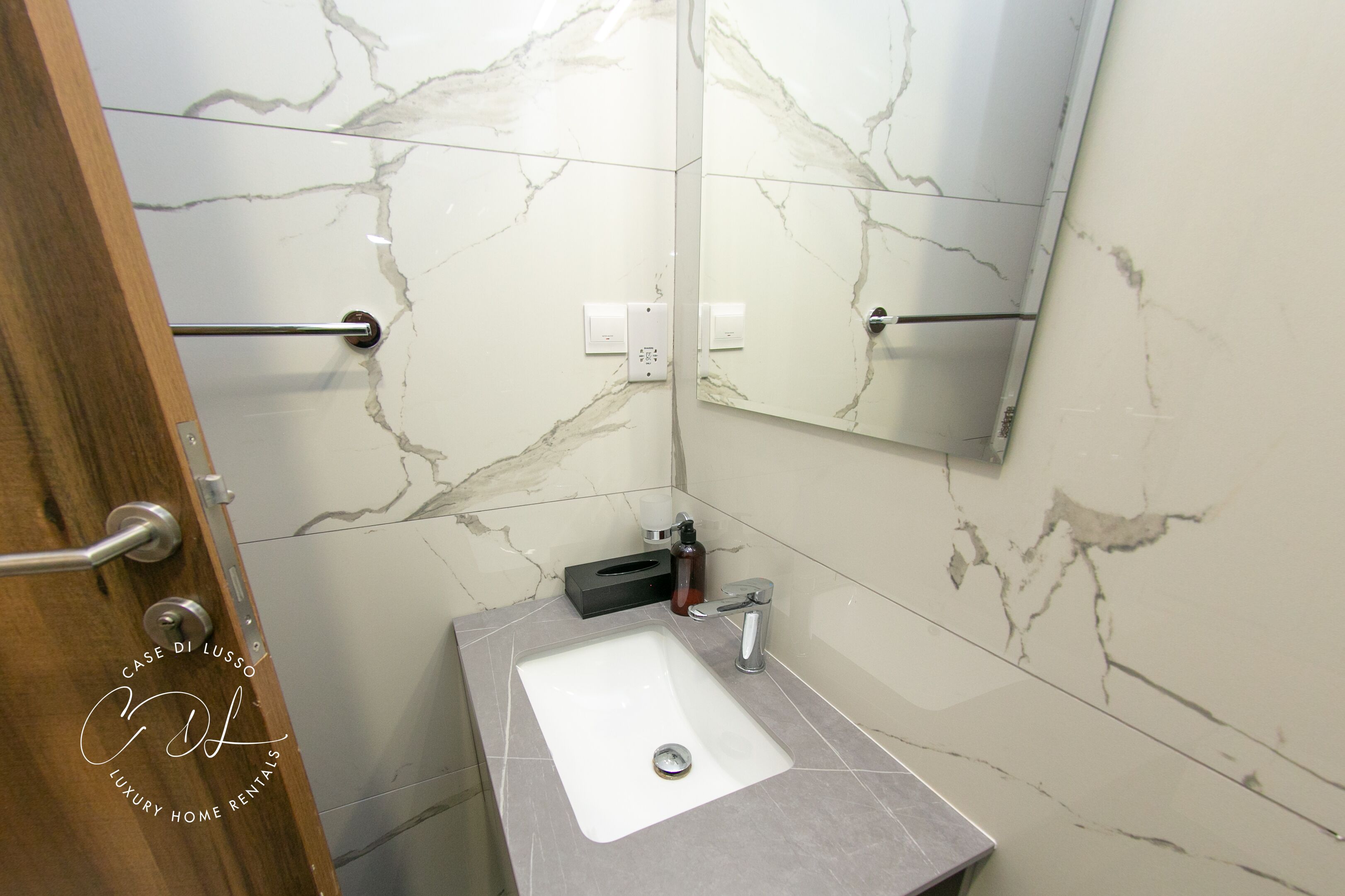 Un bagno con parete in marmo, lavabo, specchio e porta asciugamani.