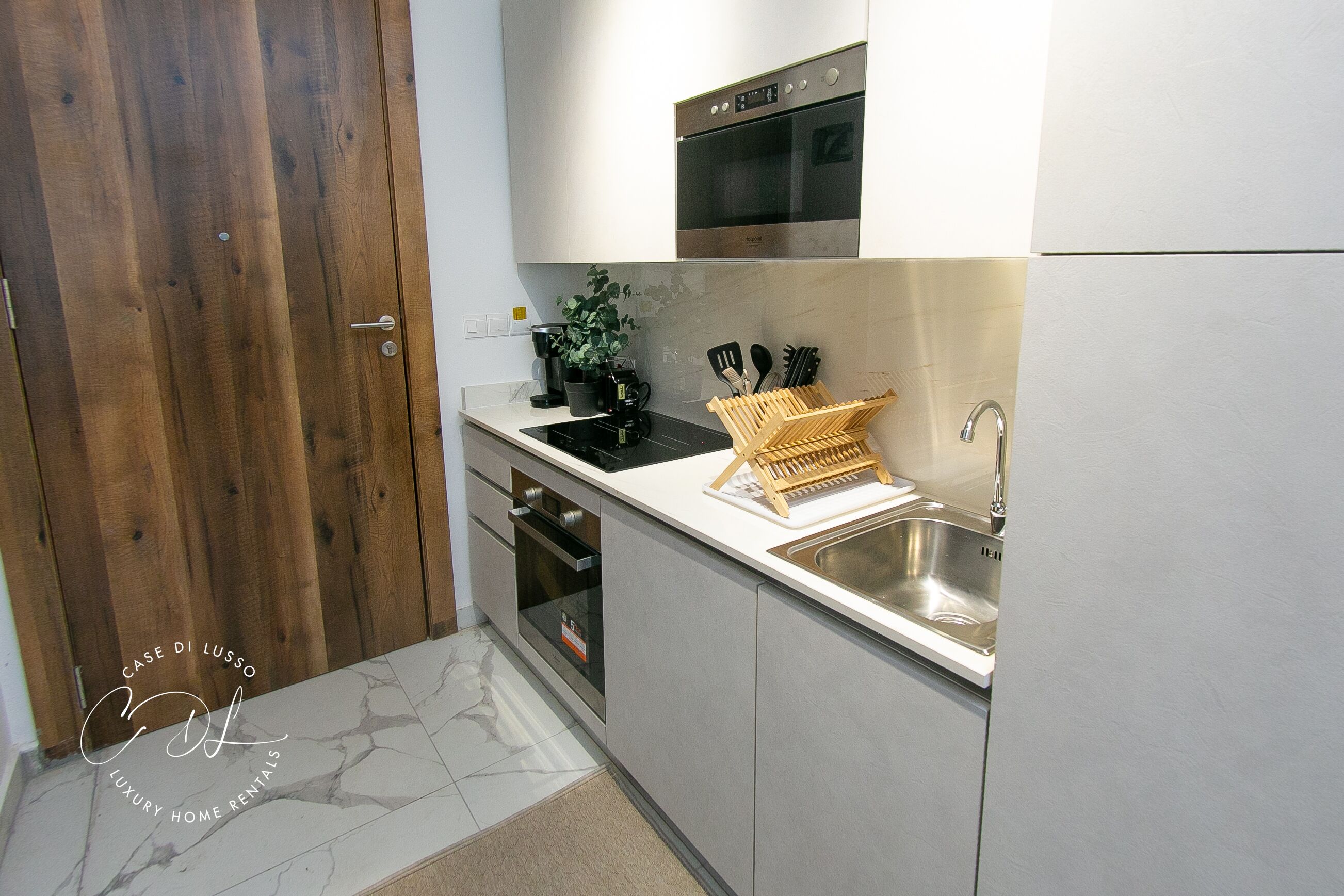 A modern kitchen with a wooden door, stainless steel appliances, and a marble backsplash.