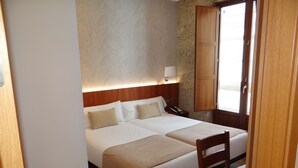 A hotel room with two beds, a wooden headboard, a bedside table with a lamp, and a window with a view. - Pensión O Códice (Santiago de Compostela)