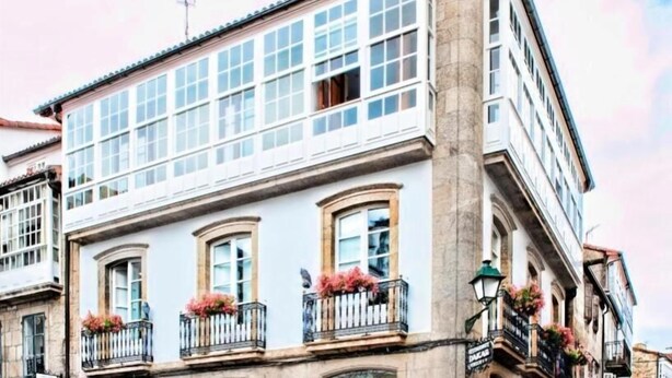 A corner building with large windows, a balcony with flowers, and a street lamp. - Pensión O Códice (Santiago de Compostela)
