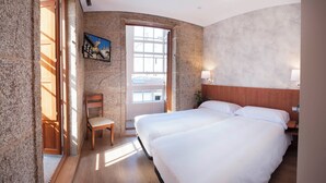 A hotel room with two beds, a wooden headboard, a chair, a painting, and a large window. - Pensión O Códice (Santiago de Compostela)