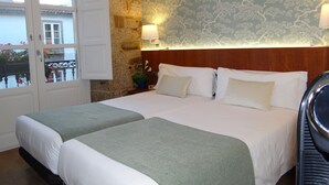 A hotel room with two beds, a stone wall, a patterned wallpaper, and a balcony with a railing. - Pensión O Códice (Santiago de Compostela)