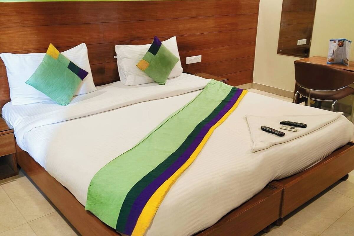 Cama bem arrumada com manta listrada em verde e amarelo, dois travesseiros e um controle remoto sobre a cama.