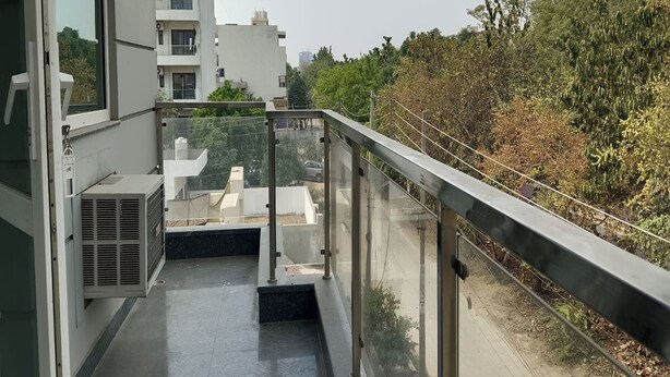 A balcony with a glass railing overlooking a road and greenery. - The Aroma Residency near The Medanta, The Medicity, Gurgaon (Gurugram)