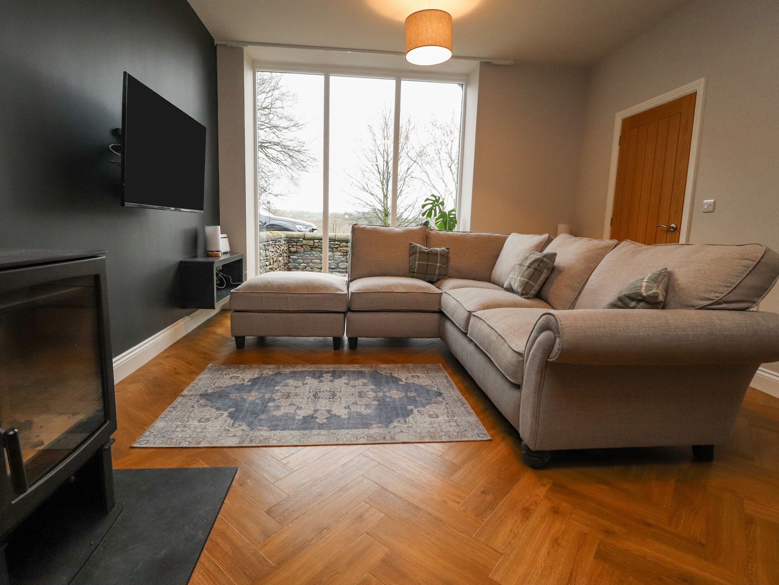 Ein Wohnzimmer mit einem Ecksofa, einem flachbildfernseher an der Wand, einem Kamin und einem großen Fenster mit Blick ins Freie.