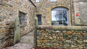 A stone building with a narrow passageway, a large arched window, and a red mailbox. - Meadow View Cottage (Carnforth)
