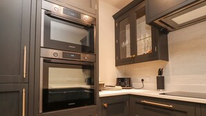 A modern kitchen with dark cabinetry, stainless steel appliances, and a white countertop. - Meadow View Cottage (Carnforth)