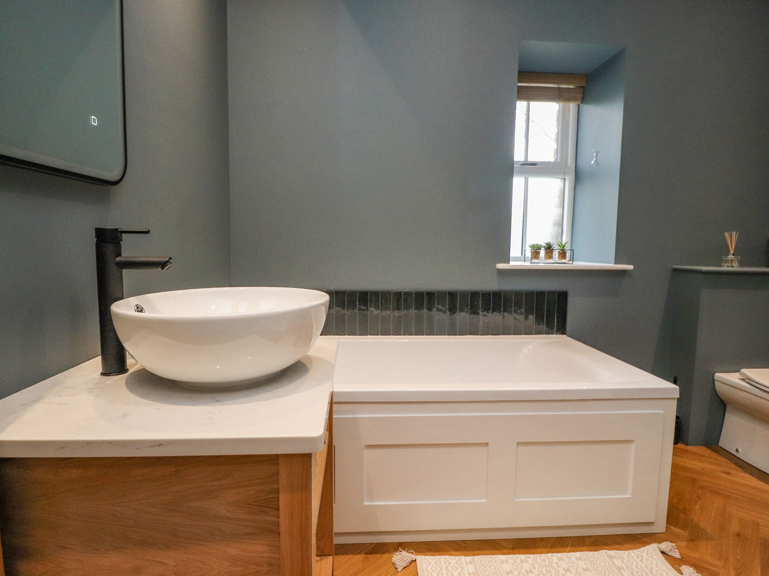Un baño con un lavamanos blanco, un grifo negro, una bañera blanca y una ventana con vistas al exterior.