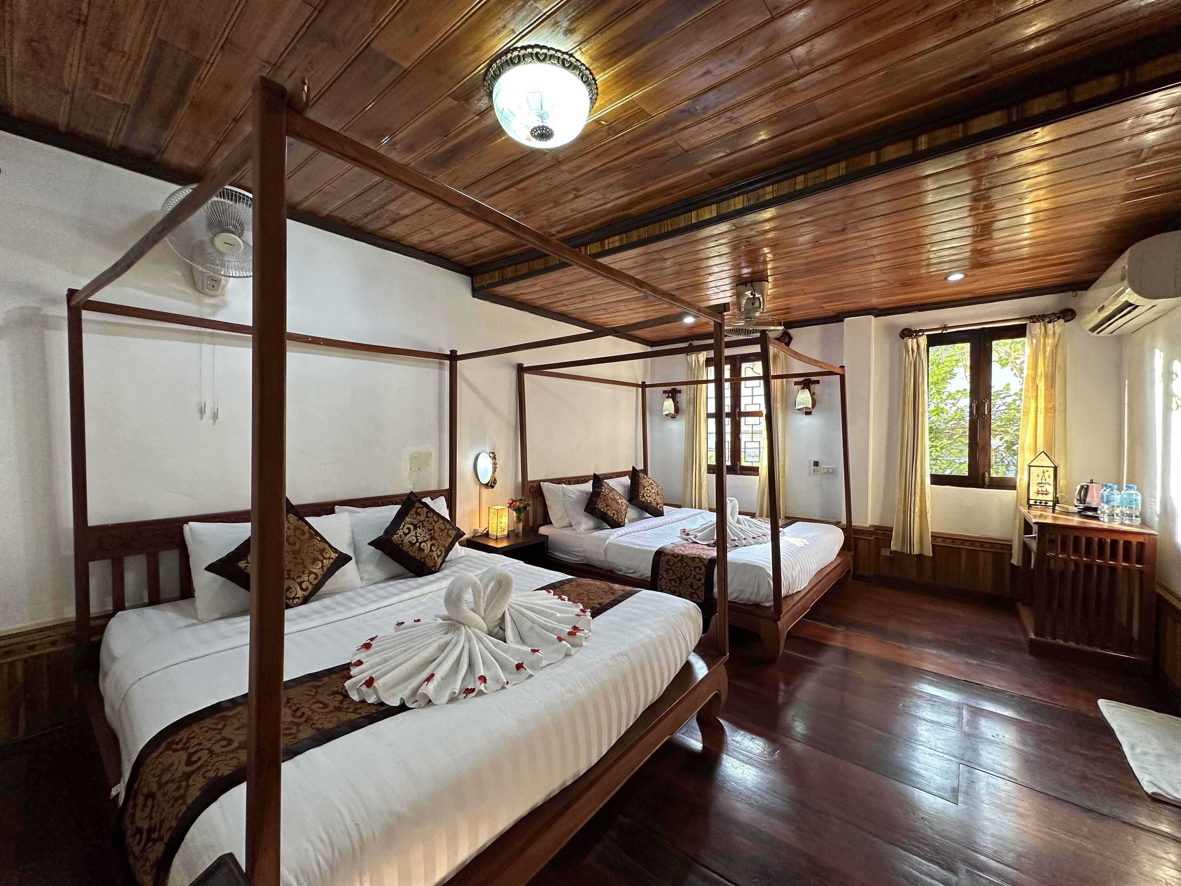 A four-poster bed with a canopy, a bedside table with a lamp, and a window with curtains.