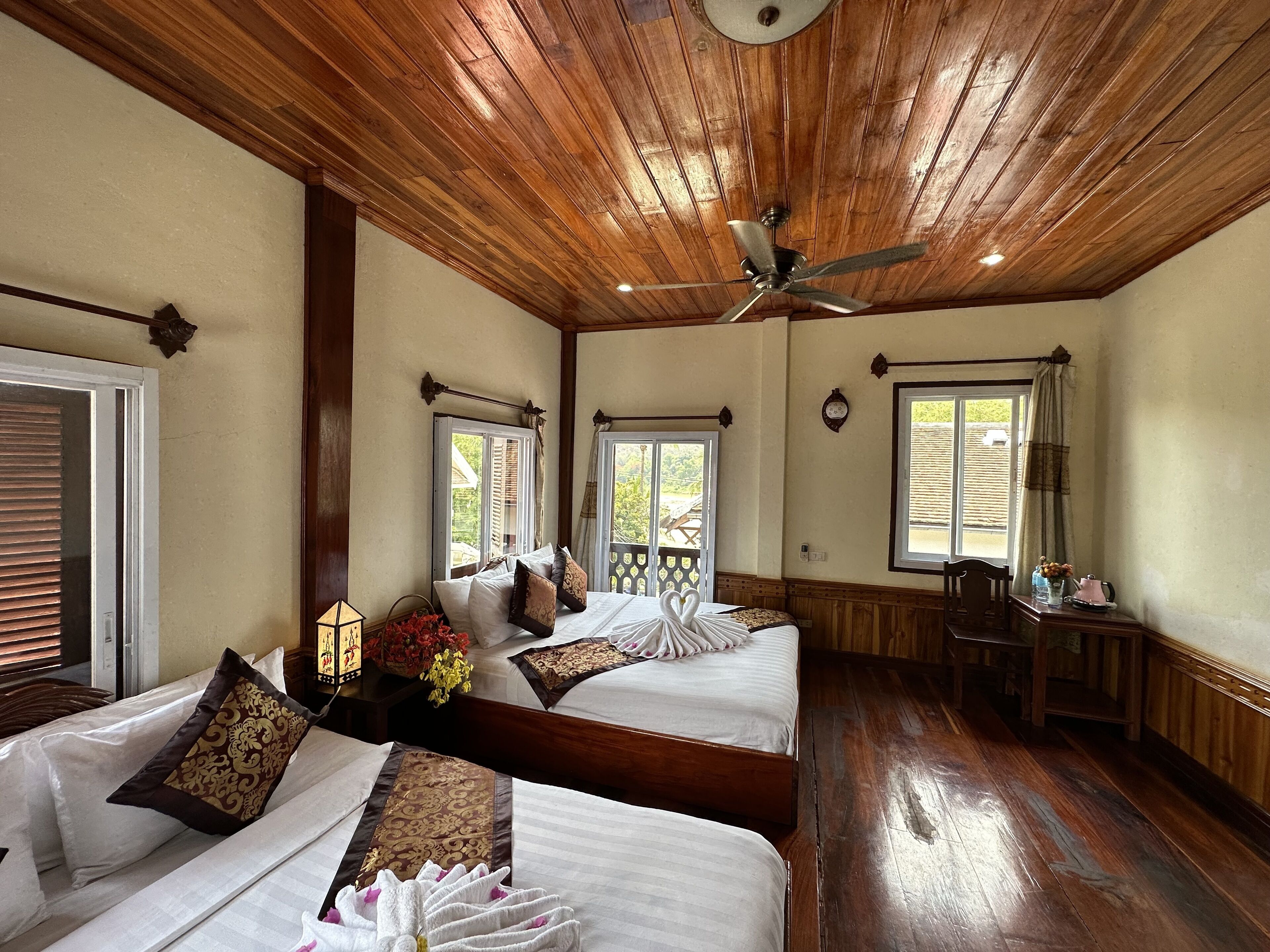 Une chambre d’hôtel avec deux lits, un plafond en bois, de grandes fenêtres et un plancher en bois.