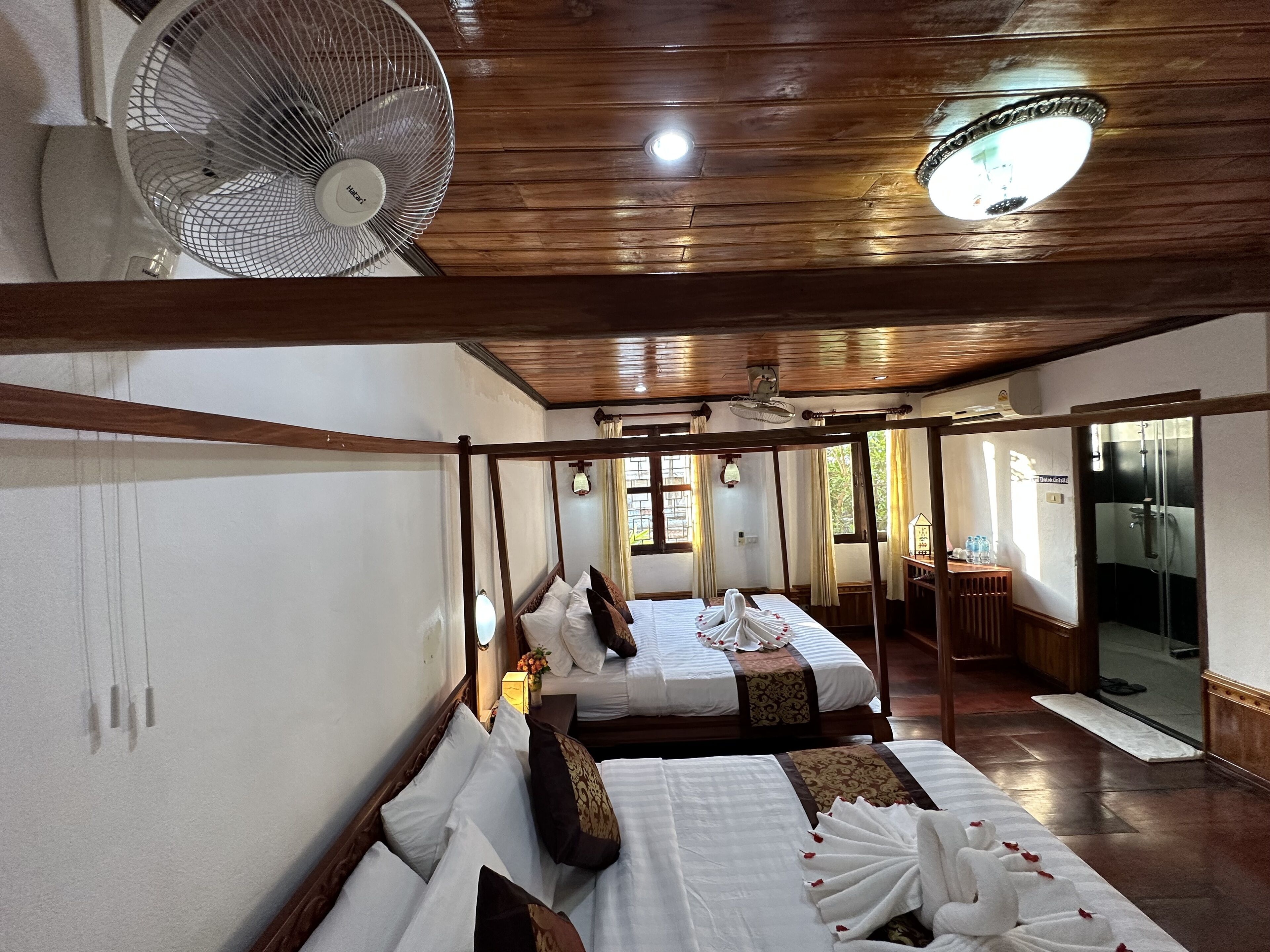 Ein Hotelzimmer mit zwei Betten, einem Deckenventilator, einem großen Spiegel und Blick ins Badezimmer.