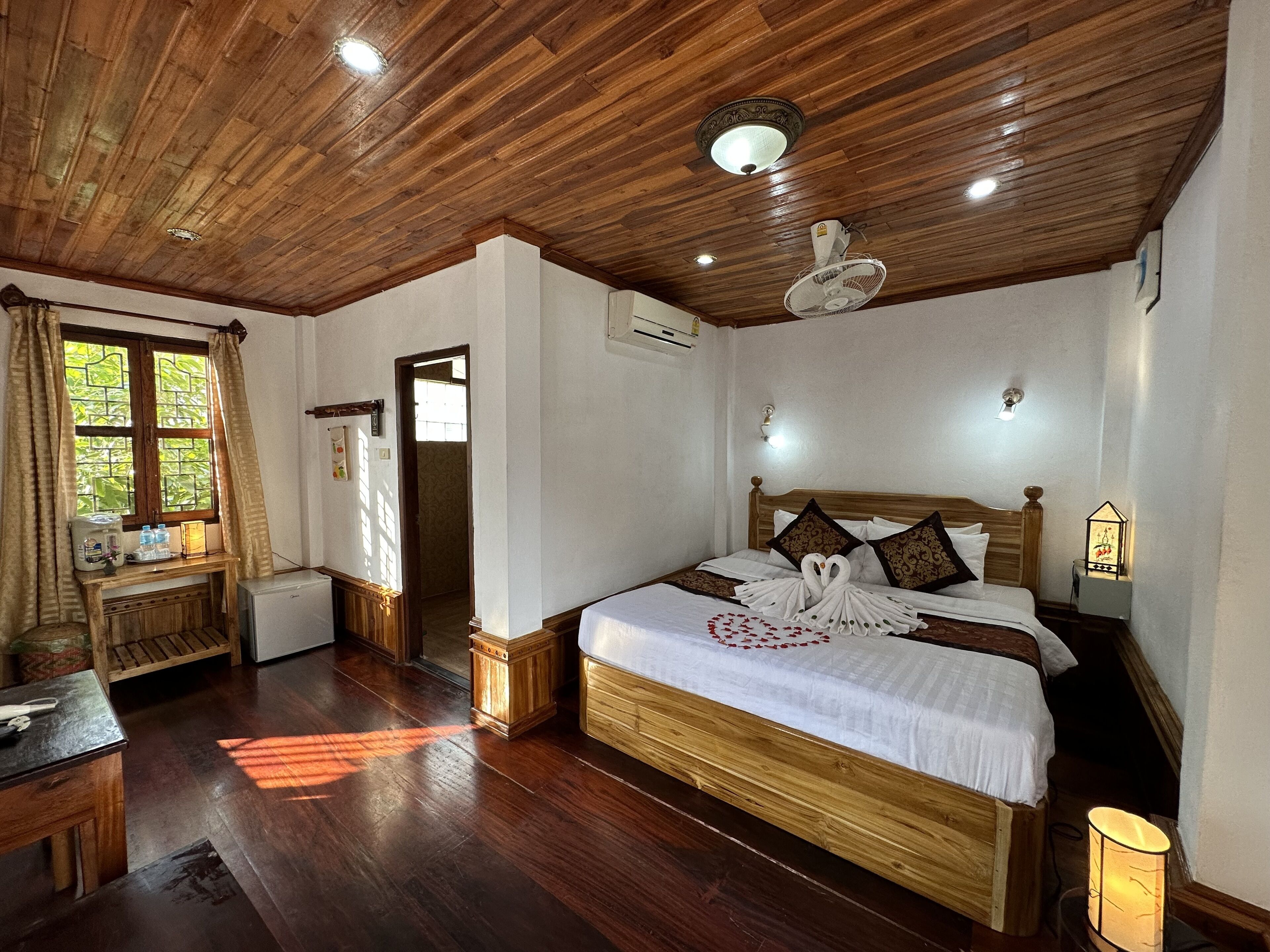 A wooden-floored bedroom with a bed, bedside lamps, and a window with curtains.