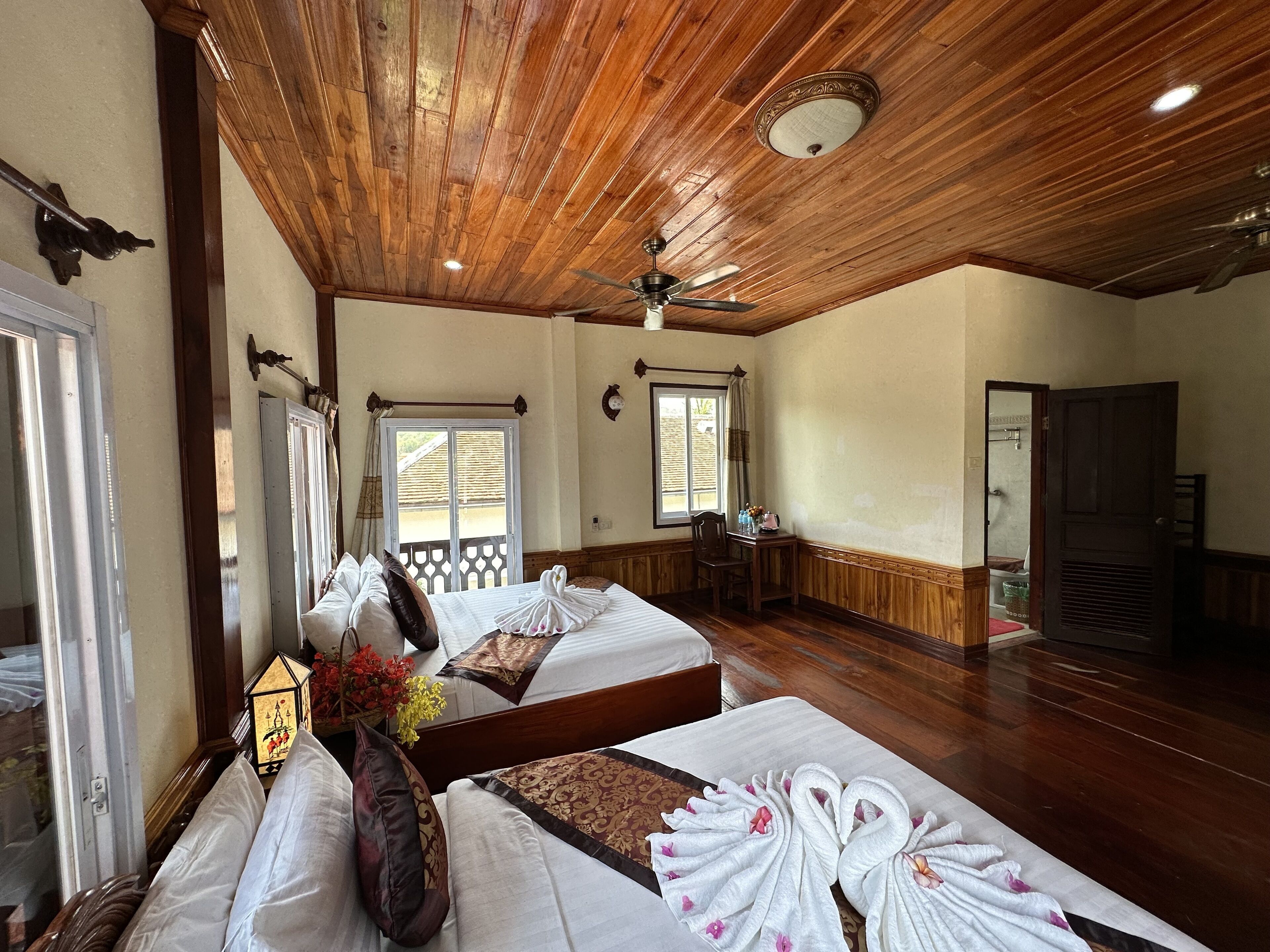 Habitación de hotel con techo de madera, una cama con ropa blanca, un escritorio de madera y una ventana con vistas.