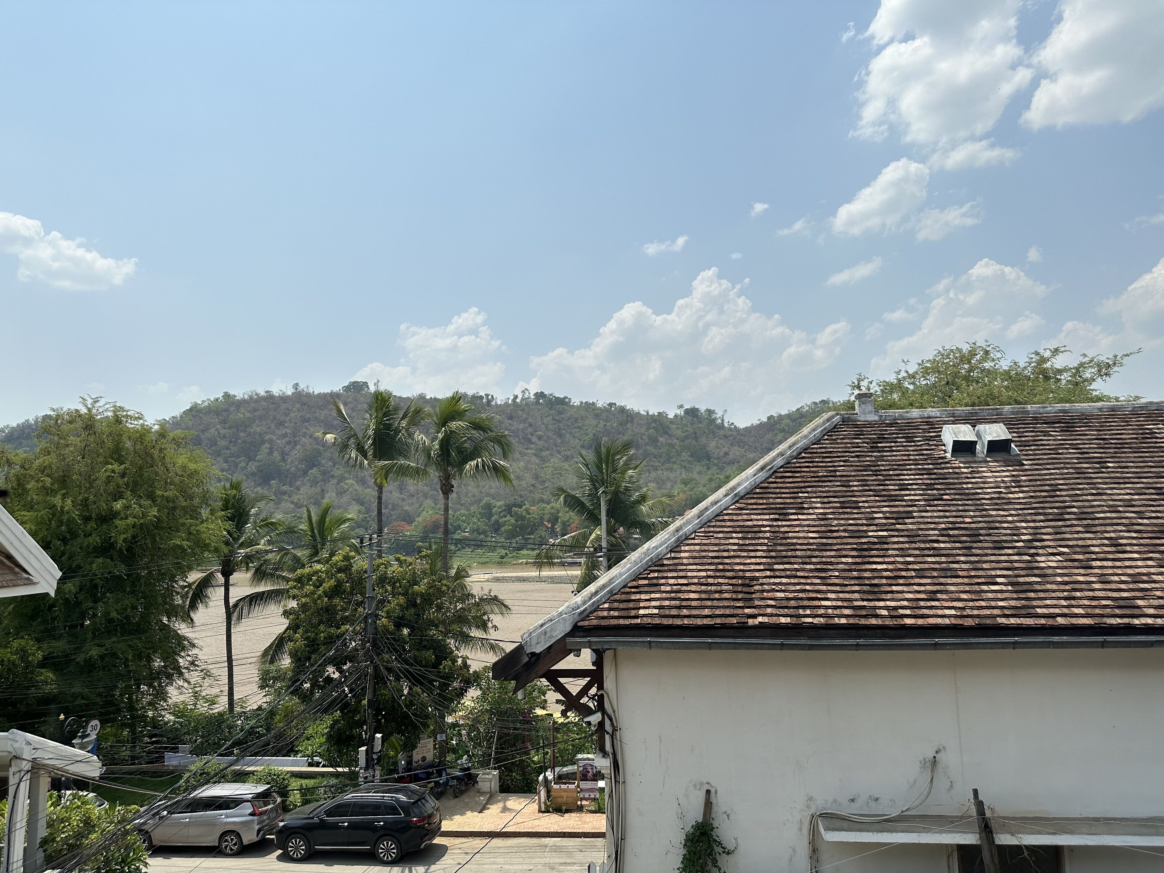 Ein Wohngebiet mit einem weißen Gebäude, einem Ziegeldach und Blick auf eine hügelige Landschaft mit Palmen.