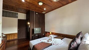 Una habitación de hotel con techo de madera, una cama con colcha blanca y marrón, un televisor sobre un mueble y un ventilador.