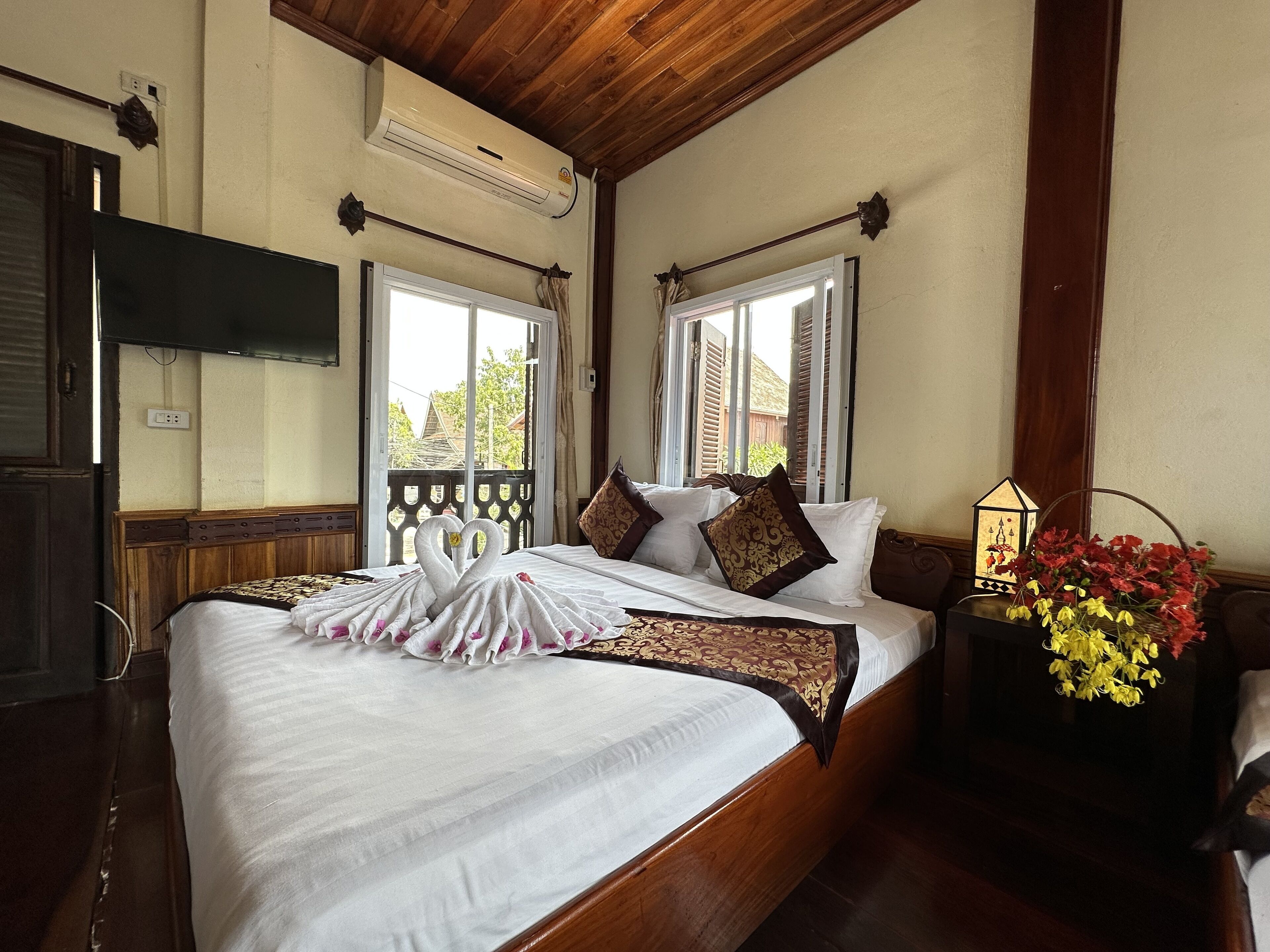 A hotel room with a large bed, a TV mounted on the wall, and a window with shutters.