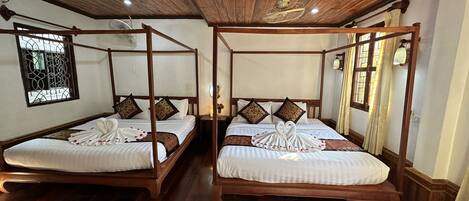 A room with two four-poster beds, wooden flooring, and a ceiling fan.