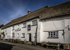 Um edifício tradicional branco com telhado de palha, uma placa com a inscrição "Duke of York" e área de estar ao ar livre.