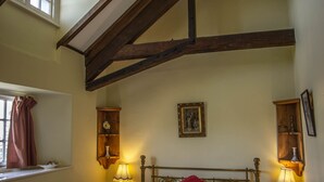 A bedroom with a bed, two bedside tables, a window with curtains, a wall-mounted picture, and a ceiling light fixture. - Duke of York (Winkleigh)