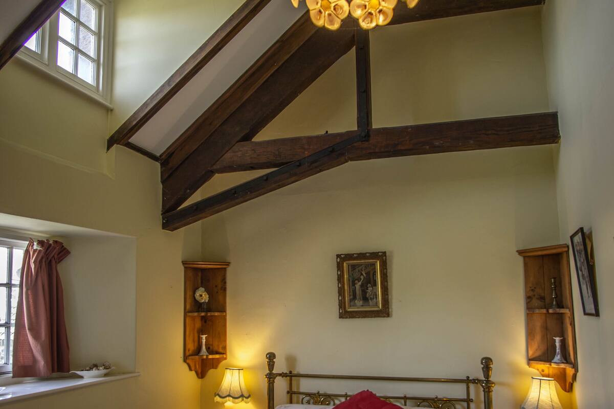 A bedroom with a bed, two bedside tables, a window with curtains, a wall-mounted picture, and a ceiling light fixture.