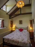 Quarto com cama, duas mesas de cabeceira, janela com cortinas, um quadro pendurado na parede e luminária no teto.