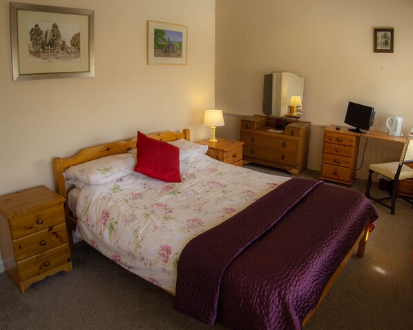 A bedroom with a bed, wooden nightstands, a dresser, a desk with a computer, and a lamp.