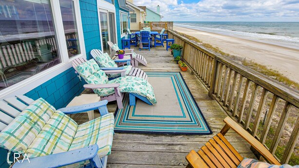 A wooden deck with outdoor seating, overlooking a beach.