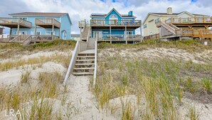 A beachfront property with a wooden staircase leading to a multi-level house with balconies.