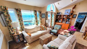A living room with a sofa, armchairs, a coffee table, a bookshelf, and a view of the ocean.