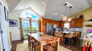 A spacious kitchen with wooden cabinets, a large island with bar stools, a dining table with chairs, and a view of the outdoors through a window.