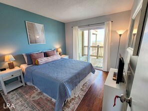 Une chambre à coucher avec un lit, des tables de chevet, une lampe, une fenêtre avec des rideaux et une vue sur l’extérieur.