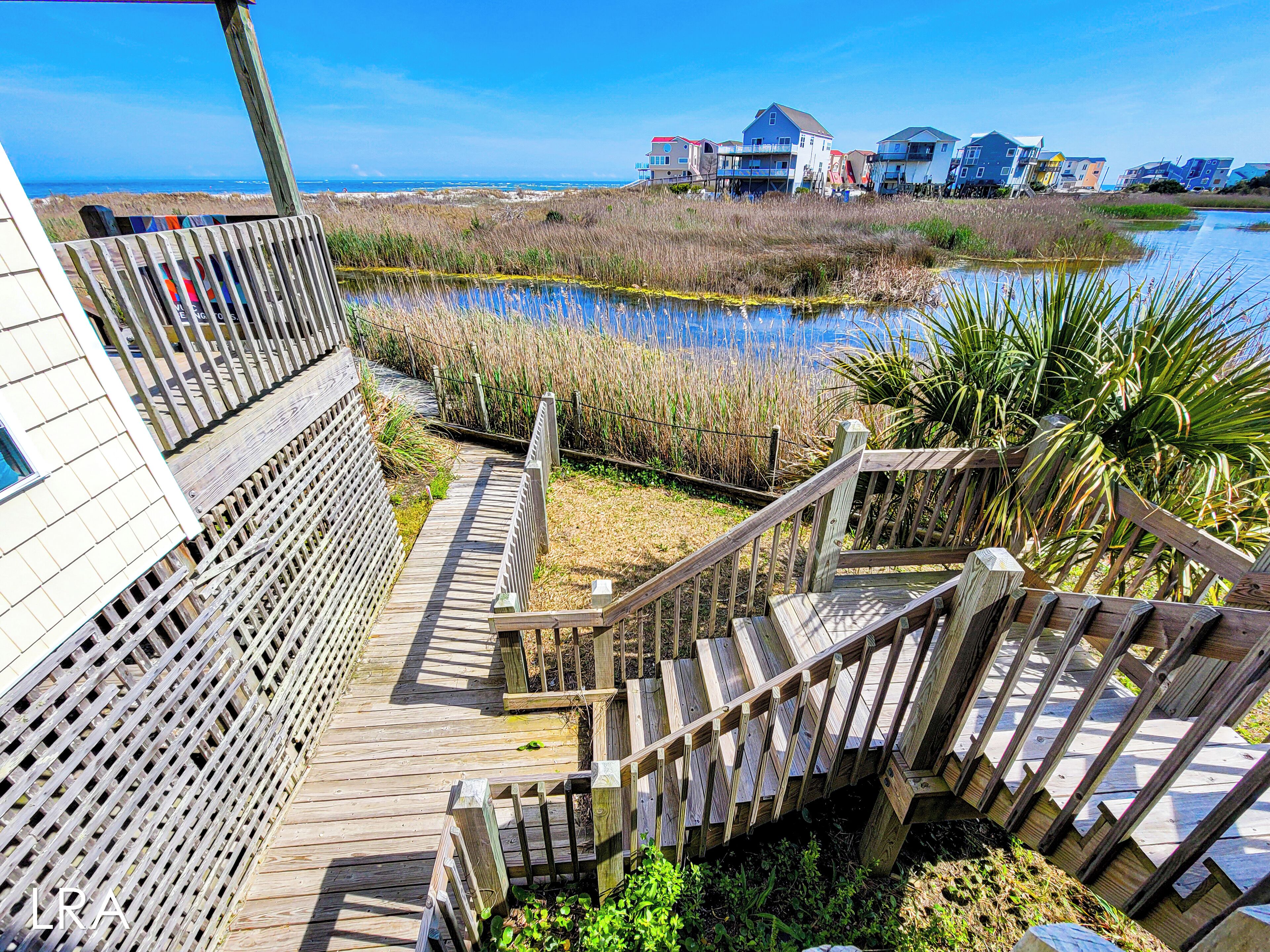 A wooden boardwalk leading to a beach with houses in the background.