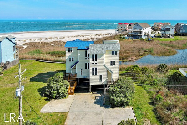 Une maison à deux étages avec un toit bleu, un porche à l’avant et une vue sur la plage et l’océan.