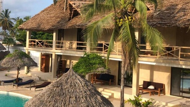 A resort with a pool, thatched-roof structures, and palm trees. - The Garden (Paje)