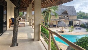 A covered outdoor area with a pool, wooden furniture, and thatched-roof structures. - The Garden (Paje)