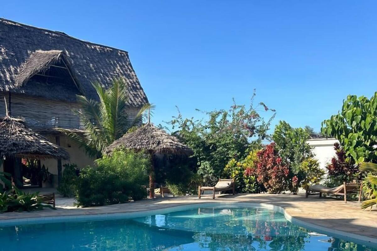 A clear blue pool surrounded by tropical vegetation and thatched-roof structures.