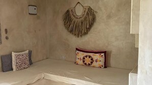 A small, cozy room with a bench, a woven wall hanging, and a patterned pillow. - The Garden (Paje)