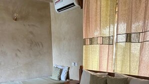 A hotel room with two beds, a window with curtains, an air conditioning unit, and a wall with a textured pattern. - The Garden (Paje)