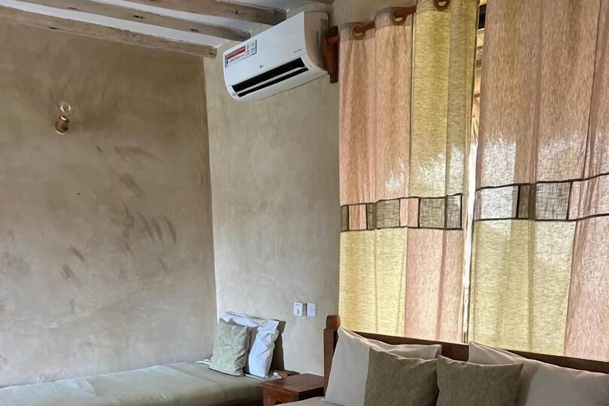 A hotel room with two beds, a window with curtains, an air conditioning unit, and a wall with a textured pattern.