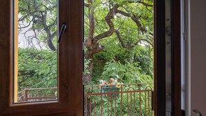 A view through a wooden door with a metal railing, leading to a balcony with lush greenery and a potted plant. - Bohemian Guest House (Sofia)