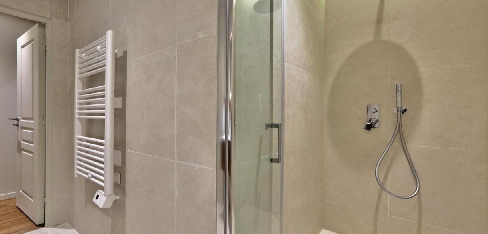 A modern bathroom with a glass shower enclosure, a white towel rack, and a handheld showerhead.