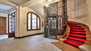 Eine prächtige Treppe mit rotem Teppich, einer Holztür und einem gläsernen Aufzug.