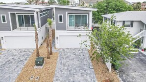 A modern two-story residential building with a flat roof, large windows, and a paved driveway.